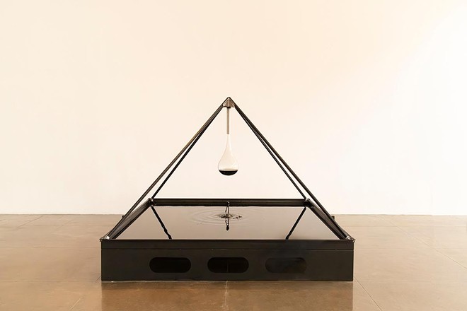 An installation from Xin Liu's "At the End of Everything" features a pyramid suspended over a fountain of oil, from which a globe containing oil is suspended. - Beth Devillier